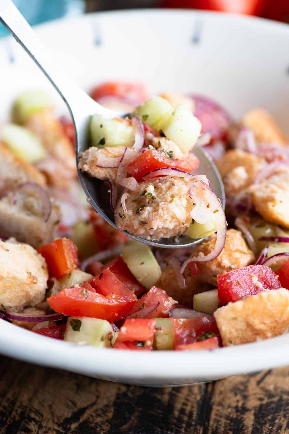 A close up of Cialledda salad with cucumber, tomatoes and bread on a serving spoon.