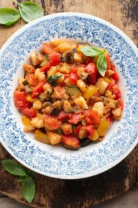 An overhead shot of Ciambotta (Italian vegetable stew) in a blue bowl, the background is wooden.