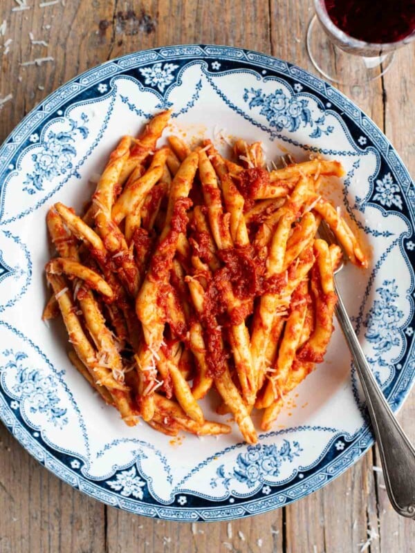 An overhead shot of spicy Nduja pasta (Fileja) in a blue and white bowl with a fork, the background is rustic wood.