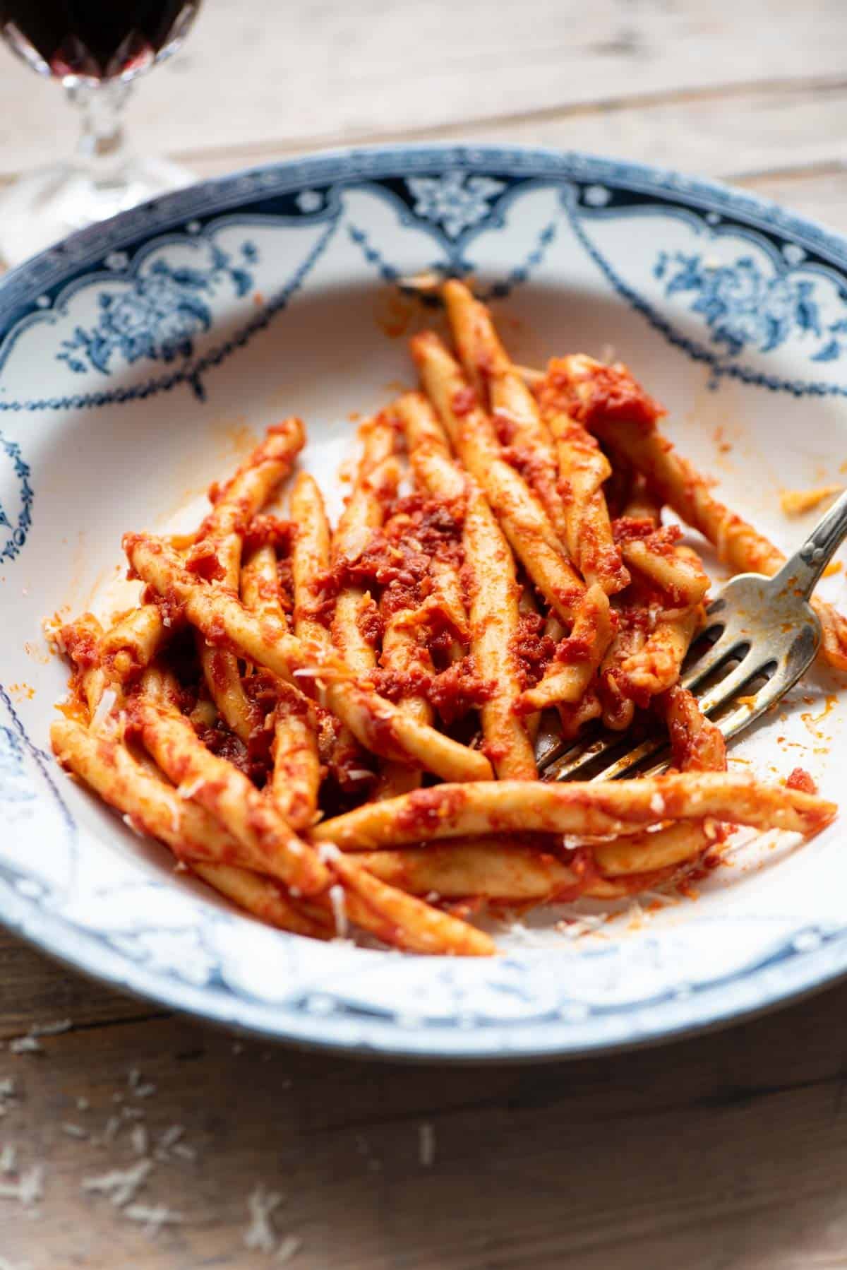 A side shot of spicy Calabrian pasta with Nduja in a blue and white bowl.