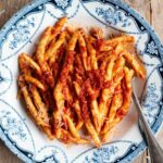 An overhead shot of a spicy tomato Nduja pasta in a blue and white bowl.