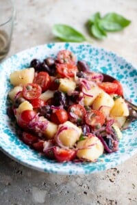 A Sicilian potato salad with olives, tomatoes and onions in a blue and white bowl.
