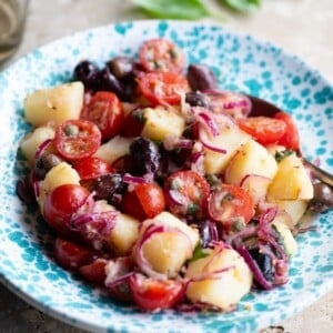 A Sicilian potato salad with olives, tomatoes and onions in a blue and white bowl.