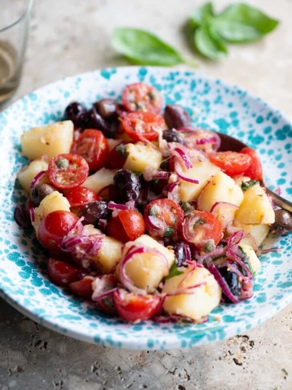 A Sicilian potato salad with olives, tomatoes and onions in a blue and white bowl.