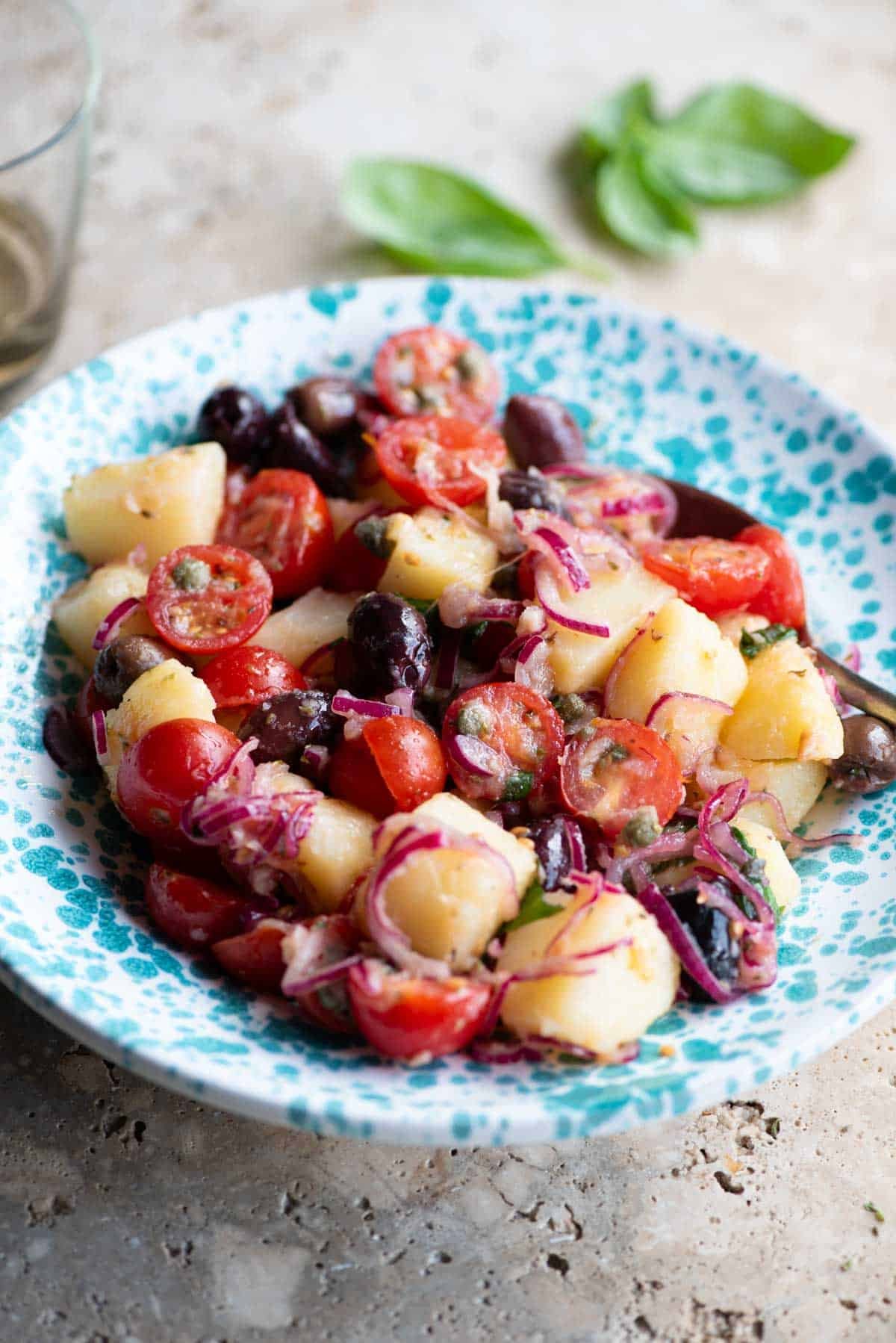 A Sicilian potato salad with olives, tomatoes and onions in a blue and white bowl.