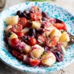 A close up cropped image of a Sicilian potato salad in a blue bowl with olives, onions and tomatoes.