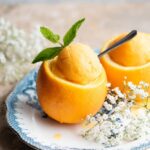 A close up cropped image of orange sorbet in a whole orange topped with a sprig of mint.