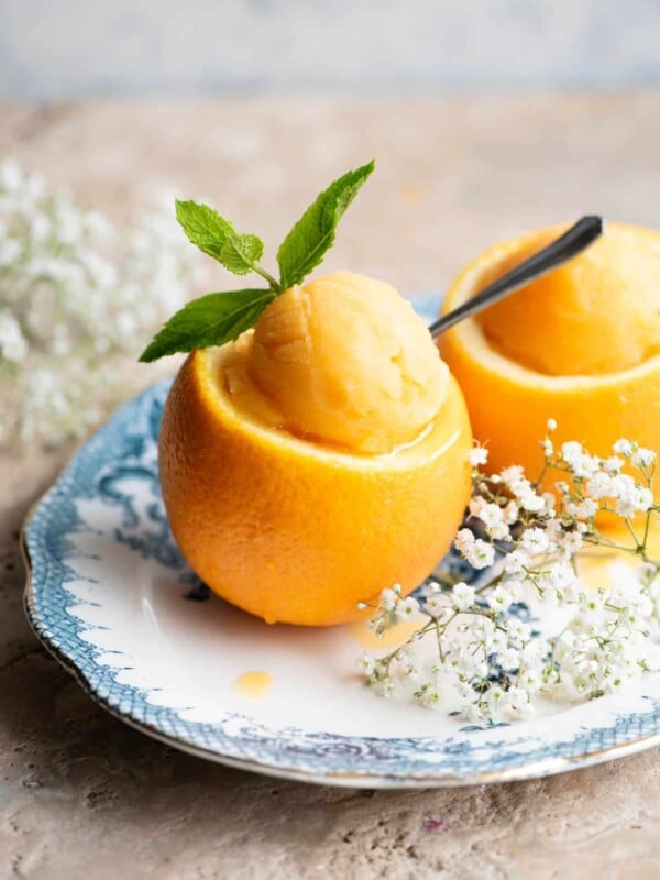 A scoop of orange sorbet served inside a hollowed out orange topped with mint leaves and a small spoon.