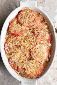 An overhead shot of an Italian potato and tomato gratin in an oval dish sitting on a Travertine background.