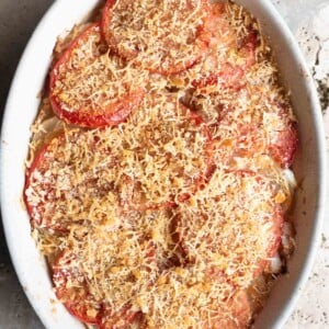 An overhead shot of an Italian potato and tomato gratin in an oval dish sitting on a Travertine background.