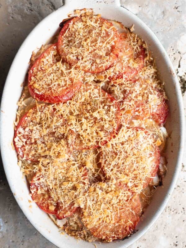 An overhead shot of an Italian potato and tomato gratin in an oval dish sitting on a Travertine background.