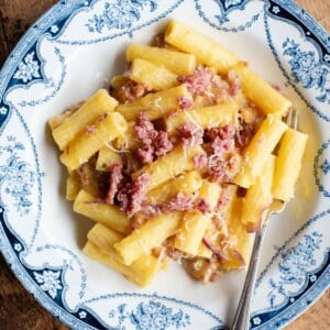 An ovehead shot of a bowl of pasta with potato, saffron and sausage, the background is wooden.