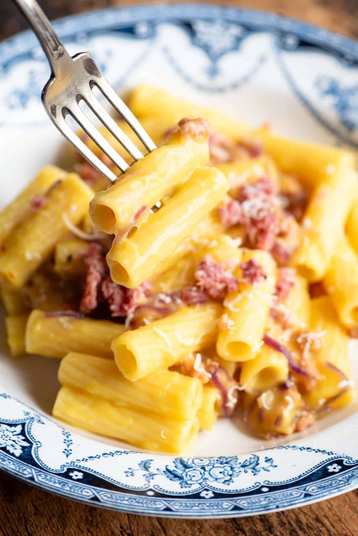 A close up of rigatoni on a fork hovering over a bowl of sausage and potato pasta.
