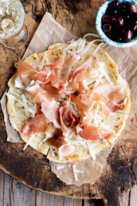 An overhead shot of Brustengo, an Italian flatbread topped with cured meat and cheese on a wooden board.