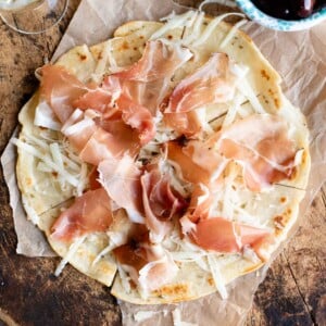 An overhead shot of Brustengo, an Italian flatbread topped with cured meat and cheese on a wooden board.