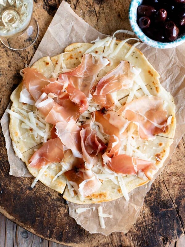 An overhead shot of Brustengo, an Italian flatbread topped with cured meat and cheese on a wooden board.