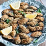 A cropped square image of mussels topped with breadcrumbs on a serving platter.