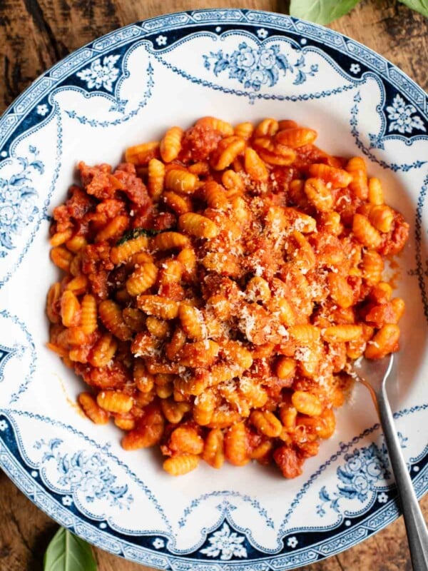 An overhead shot of a Sardinian sausage ragu (Malloreddus alla Campidanese) in a blue and white bowl on a rustic wooden background.