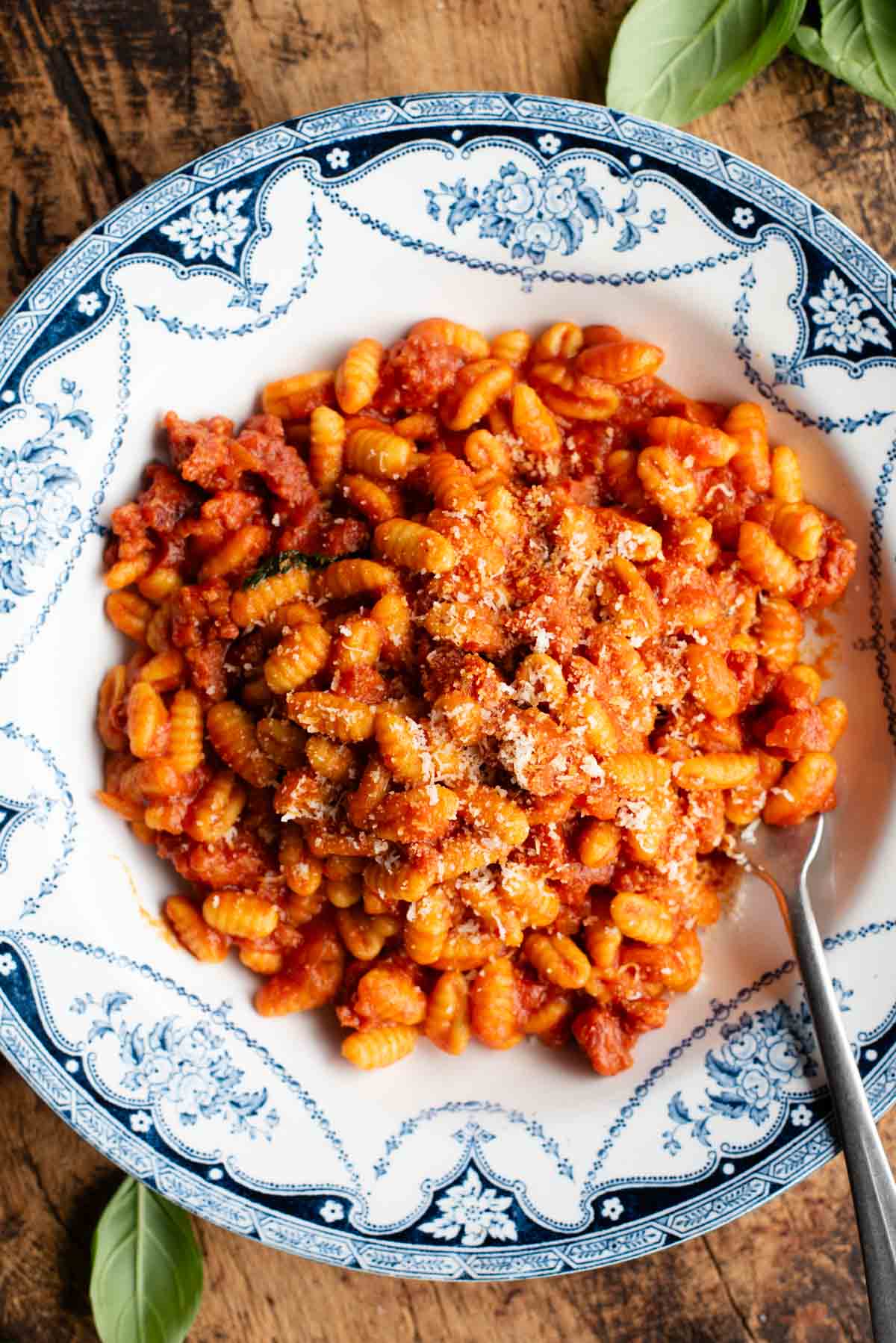 An overhead shot of a Sardinian sausage ragu (Malloreddus alla Campidanese) in a blue and white bowl on a rustic wooden background.