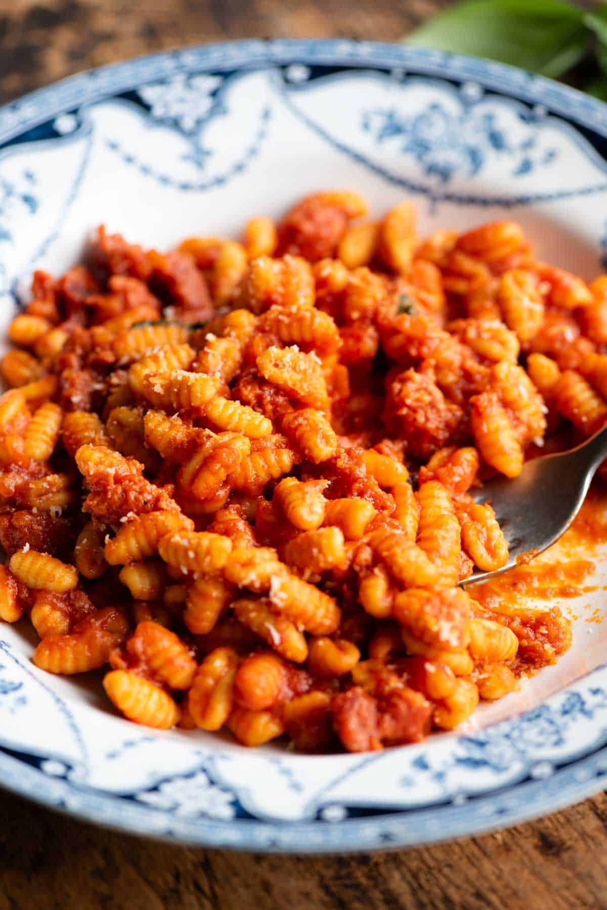 A close up side shot of a Sardinian sausage pasta in a blue and white bowl with a fork.