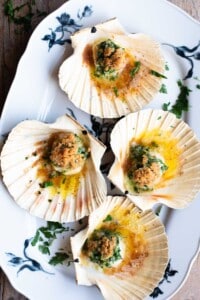 An overhead shot of four scallops in their shells sitting on a white serving platter.