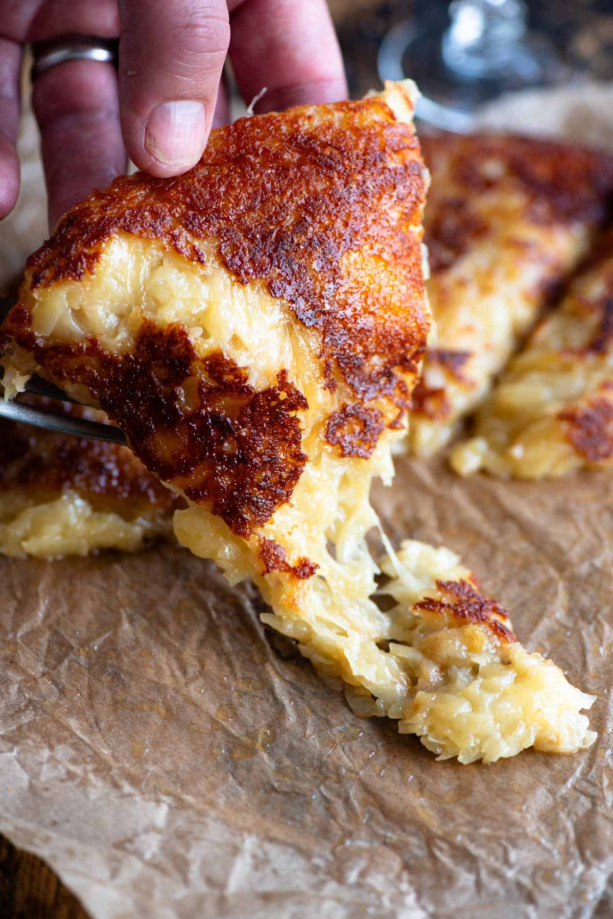 A hand picking up a slice of fried cheese and potato (frico) from a wooden board.