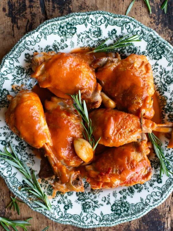 An overhead shot of chicken thighs and drumsticks on a green patterned plate with rosemary and garlic.