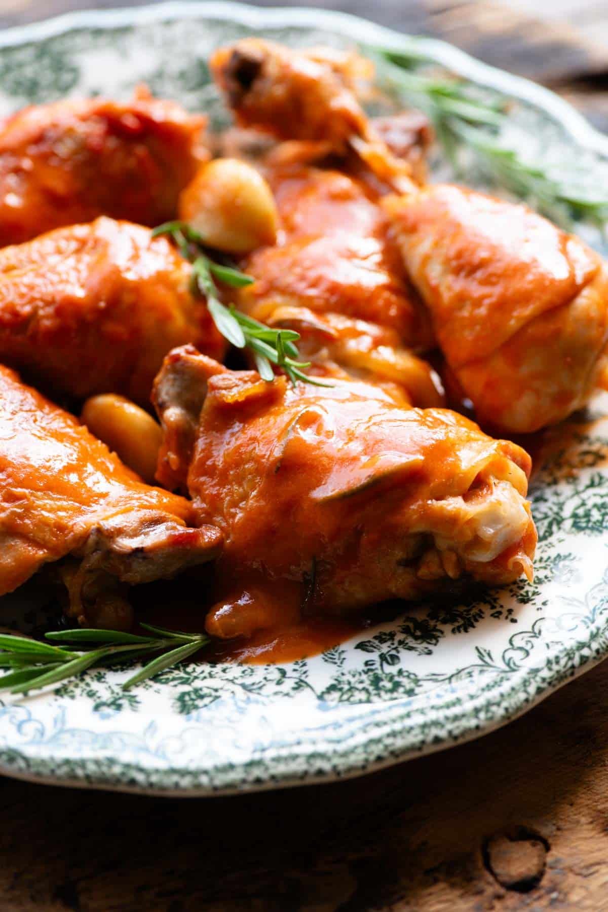 A close up side shot of a chicken thigh in tomato sauce (Pollo in Potacchio) on a green and white plate.