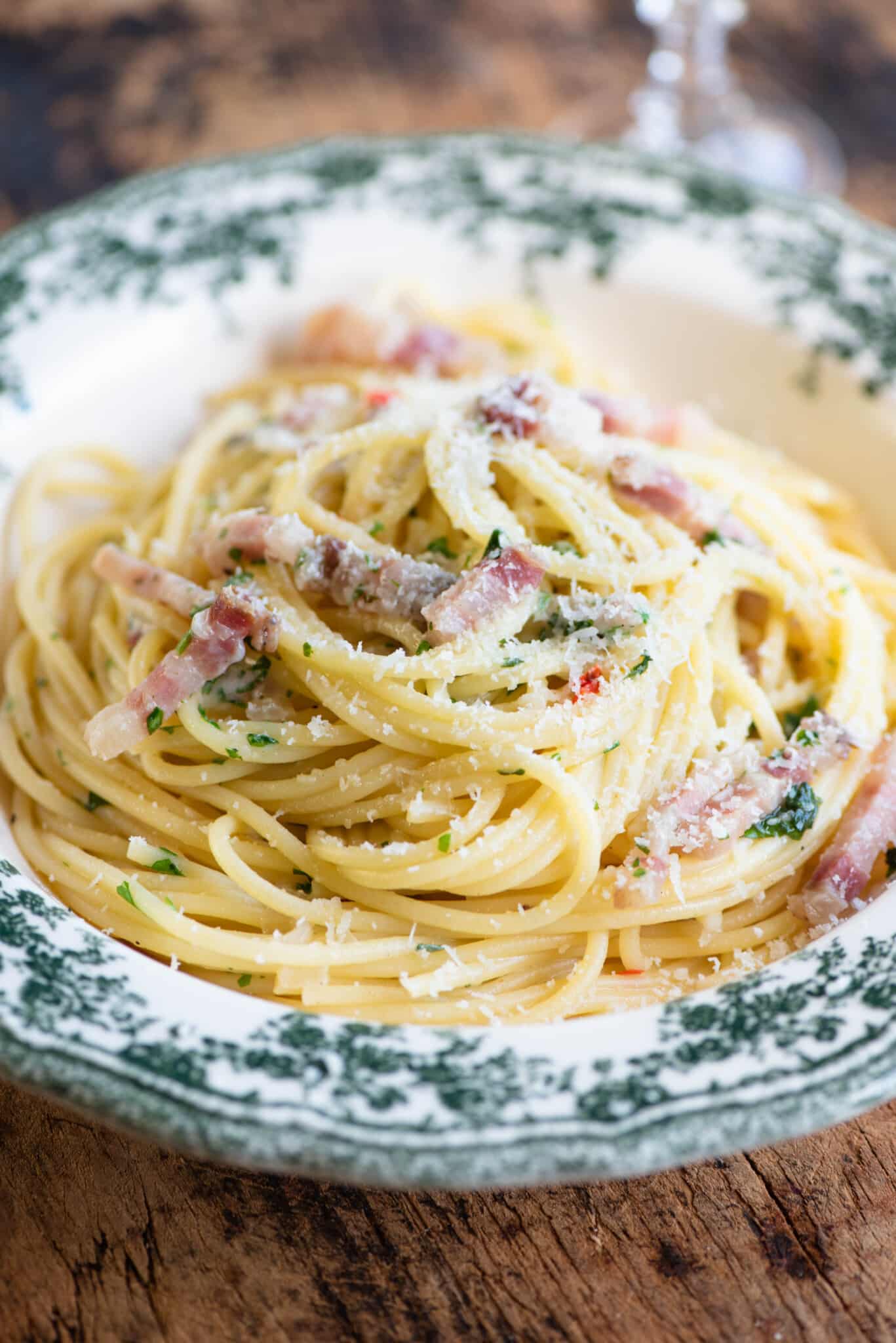 A close up of spaghetti topped with pancetta and onions in a green patterned bowl.