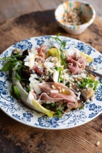 A close up of an eggplant and farro salad on a blue patterned plate on a wooden table.