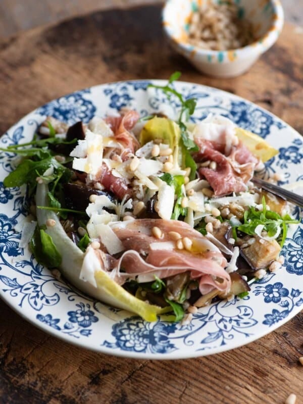 A close up of an eggplant and farro salad on a blue patterned plate on a wooden table.