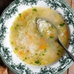 A cropped close up of rice soup in a green and white bowl with a spoon inside.