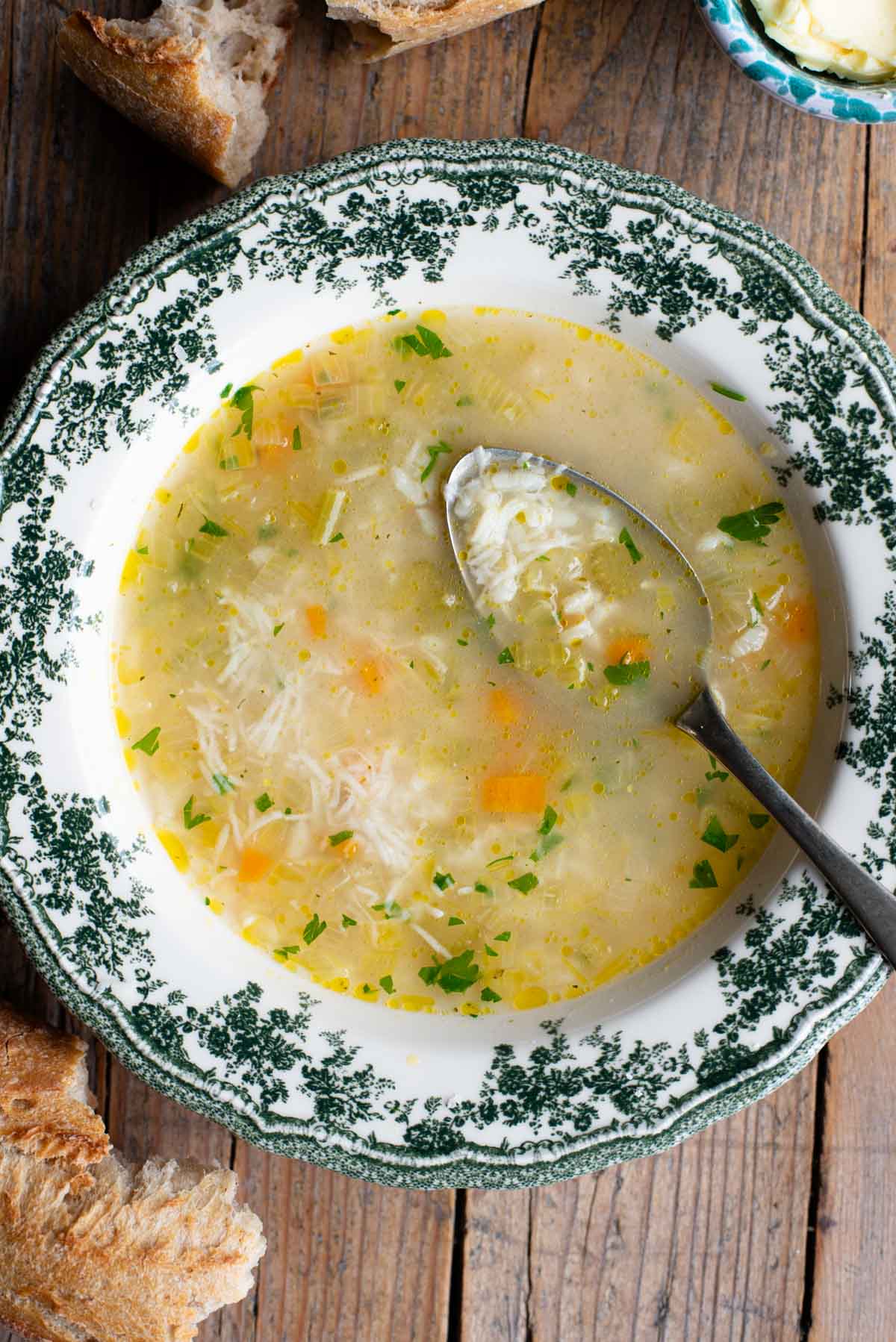An overhead shot of an Italian rice soup in a green and white bowl with a spoon inside.