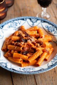 Rigatoni pasta with zozzona sauce in a blue and white patterned bowl sitting on a wooden table.