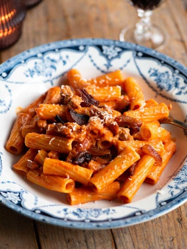 Rigatoni pasta with zozzona sauce in a blue and white patterned bowl sitting on a wooden table.