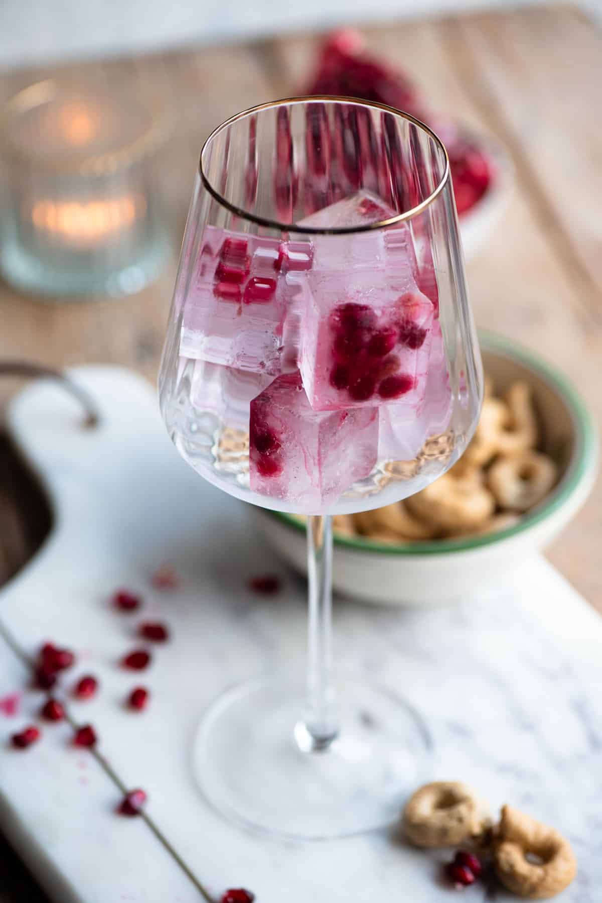 A wine glass with a gold rim filled with pomegranate ice cubes.