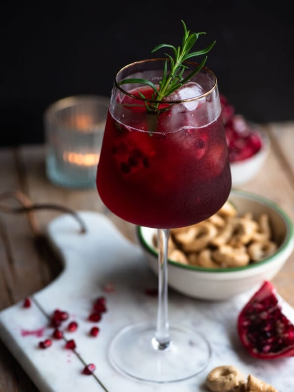 A pomegranate spritz in a tall wine glass with a gold rim and a sprig of rosemary inside.