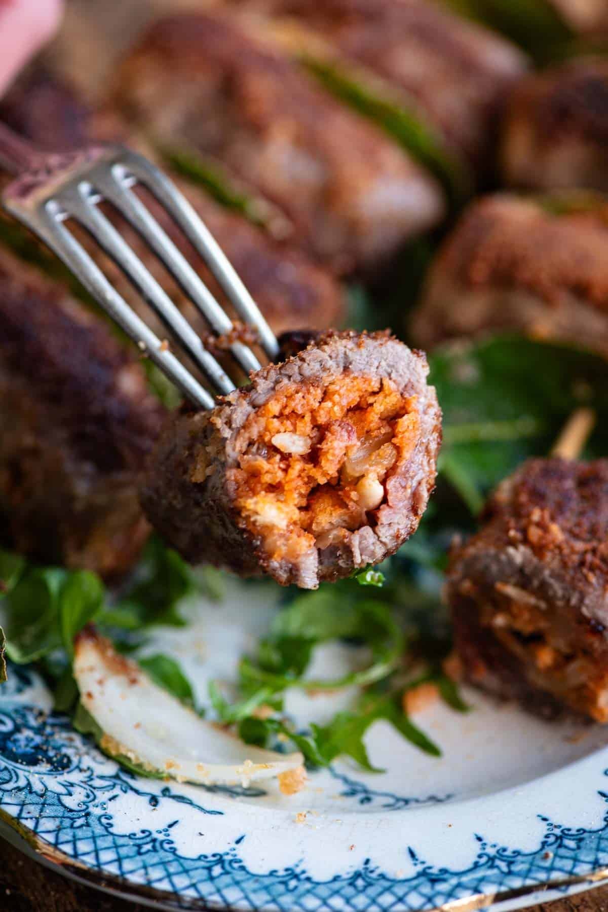 A close up of one Sicilian stuffed beef roll cut in half on a fork.