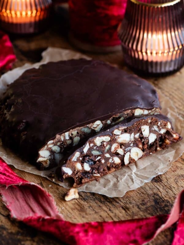 Panpepato cut into slices sitting on a wooden board with christmas red ribbon and candles.