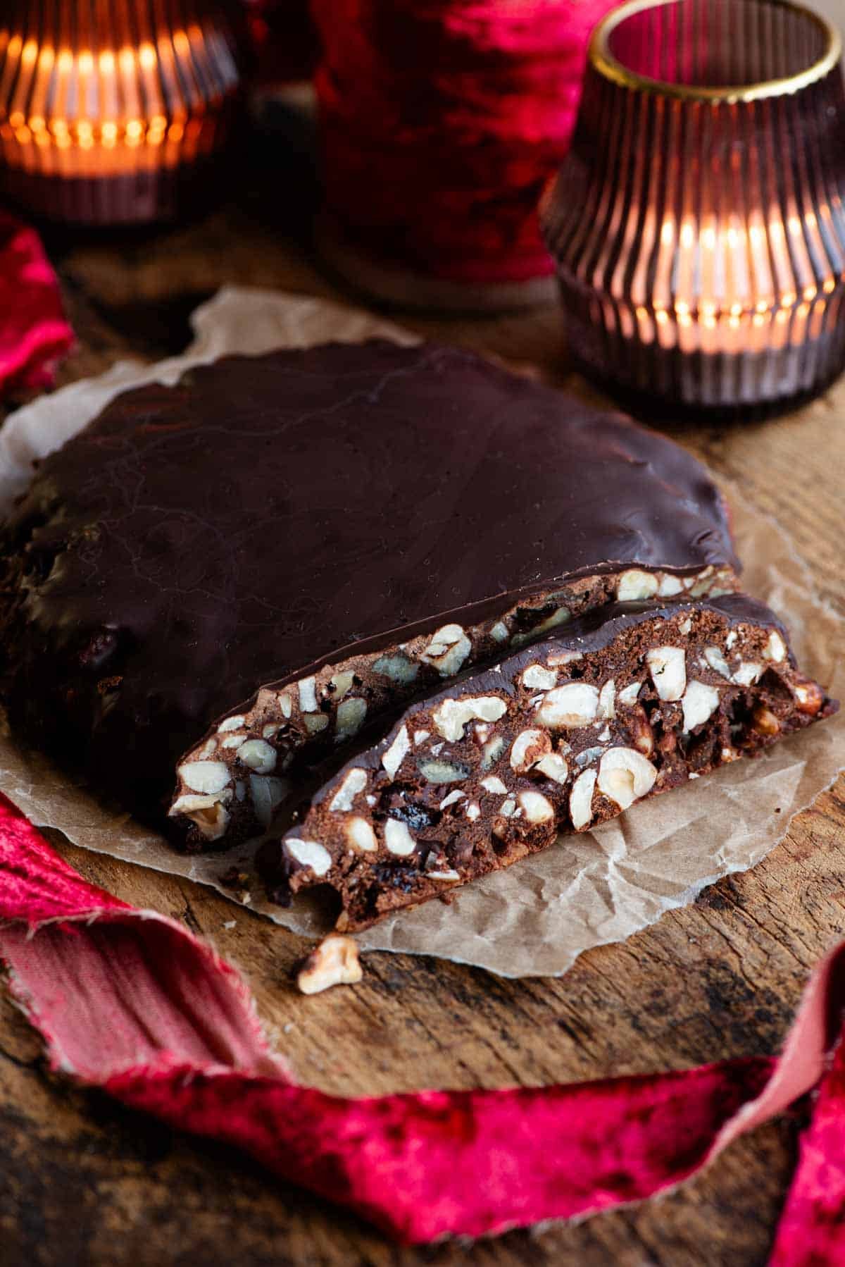 Panpepato cut into slices sitting on a wooden board with christmas red ribbon and candles.