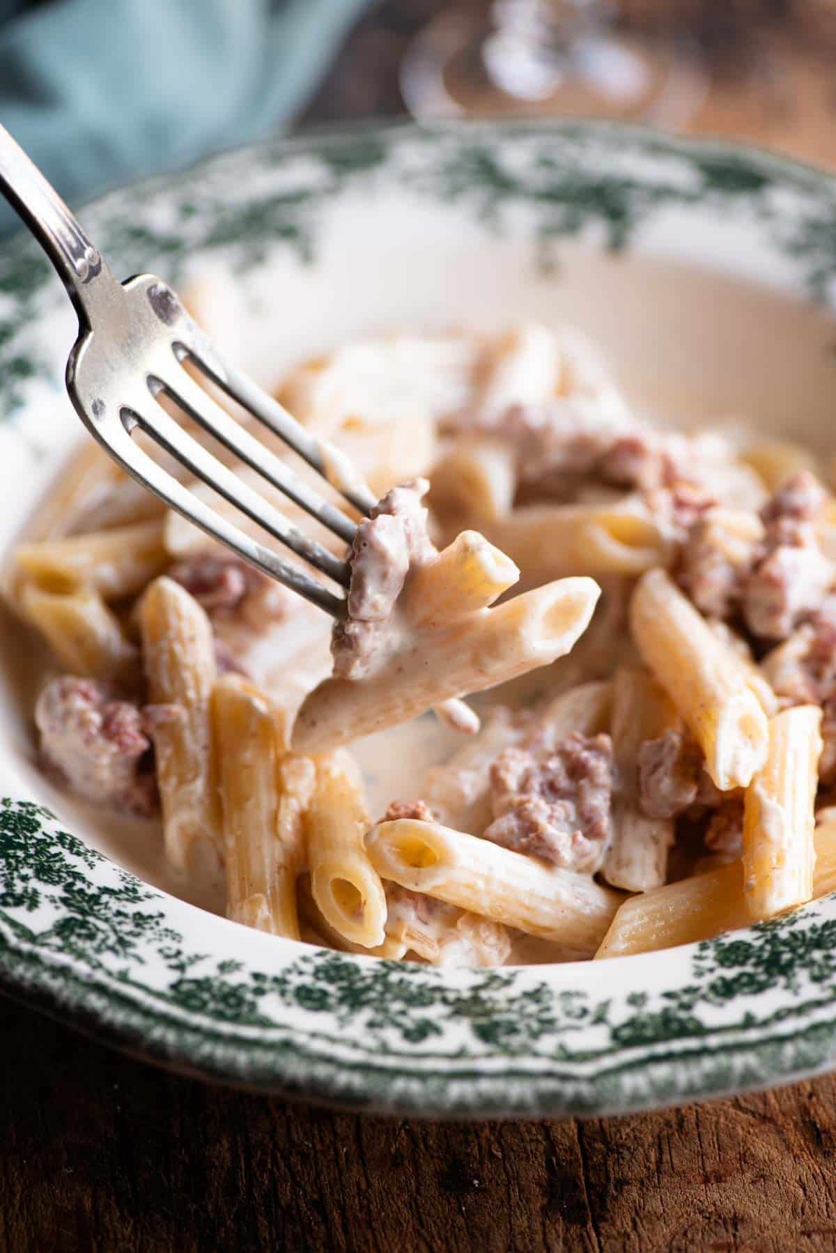 A close up of a fork picking up a bite of creamy sausage pasta.