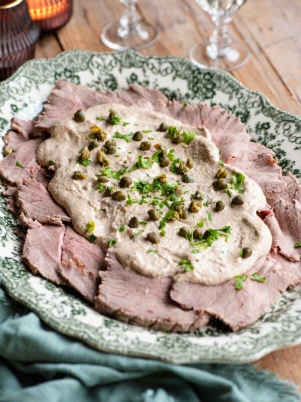 Vitello Tonnato on a serving platter topped with sauce, capers and parsley.