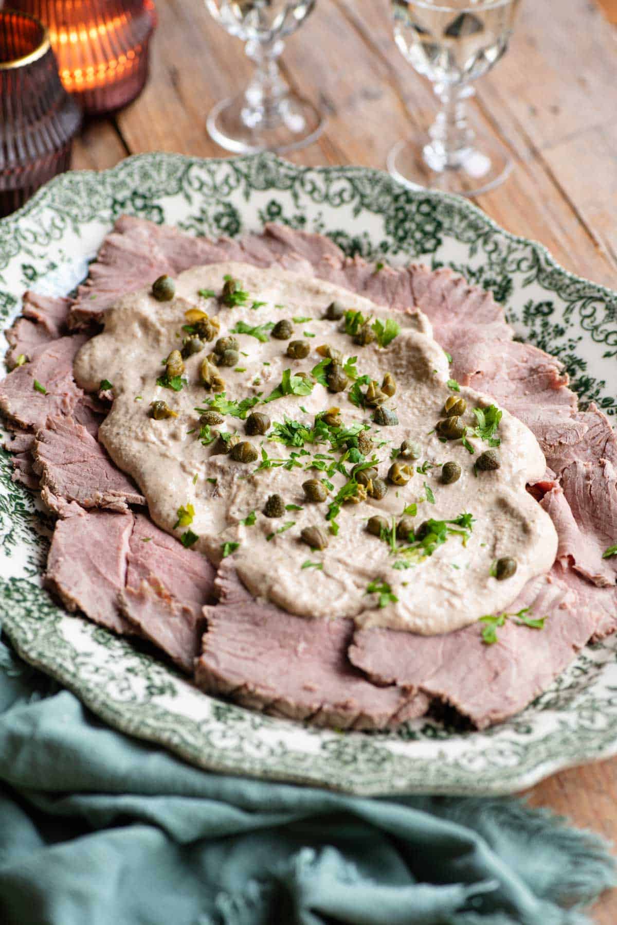 Vitello Tonnato on a serving platter topped with sauce, capers and parsley.