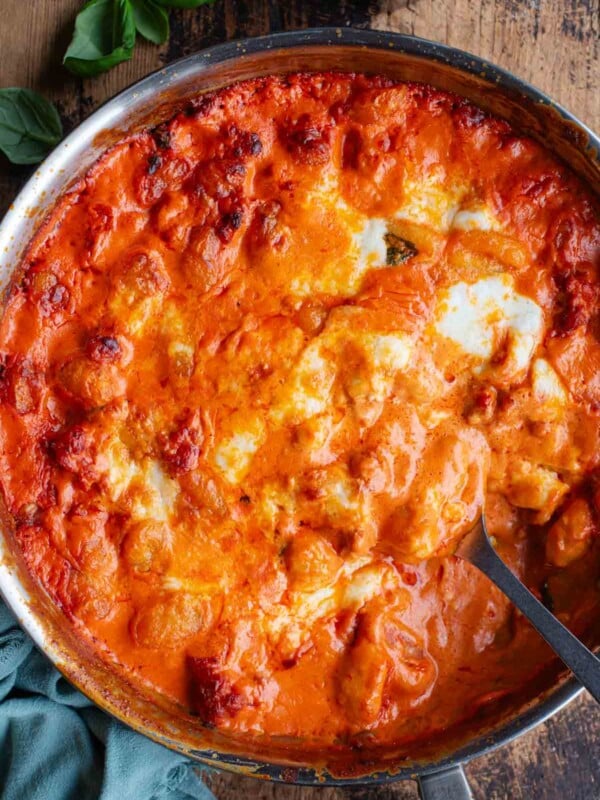 An overhead shot of spicy and creamy baked gnocchi in a skillet pan sitting on a wooden surface.