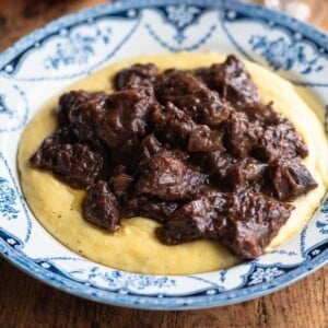 A close up cropped image of Carbonade beef stew on top of polenta.