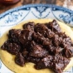 An Italian red wine beef stew on top of polenta in a blue and white bowl.