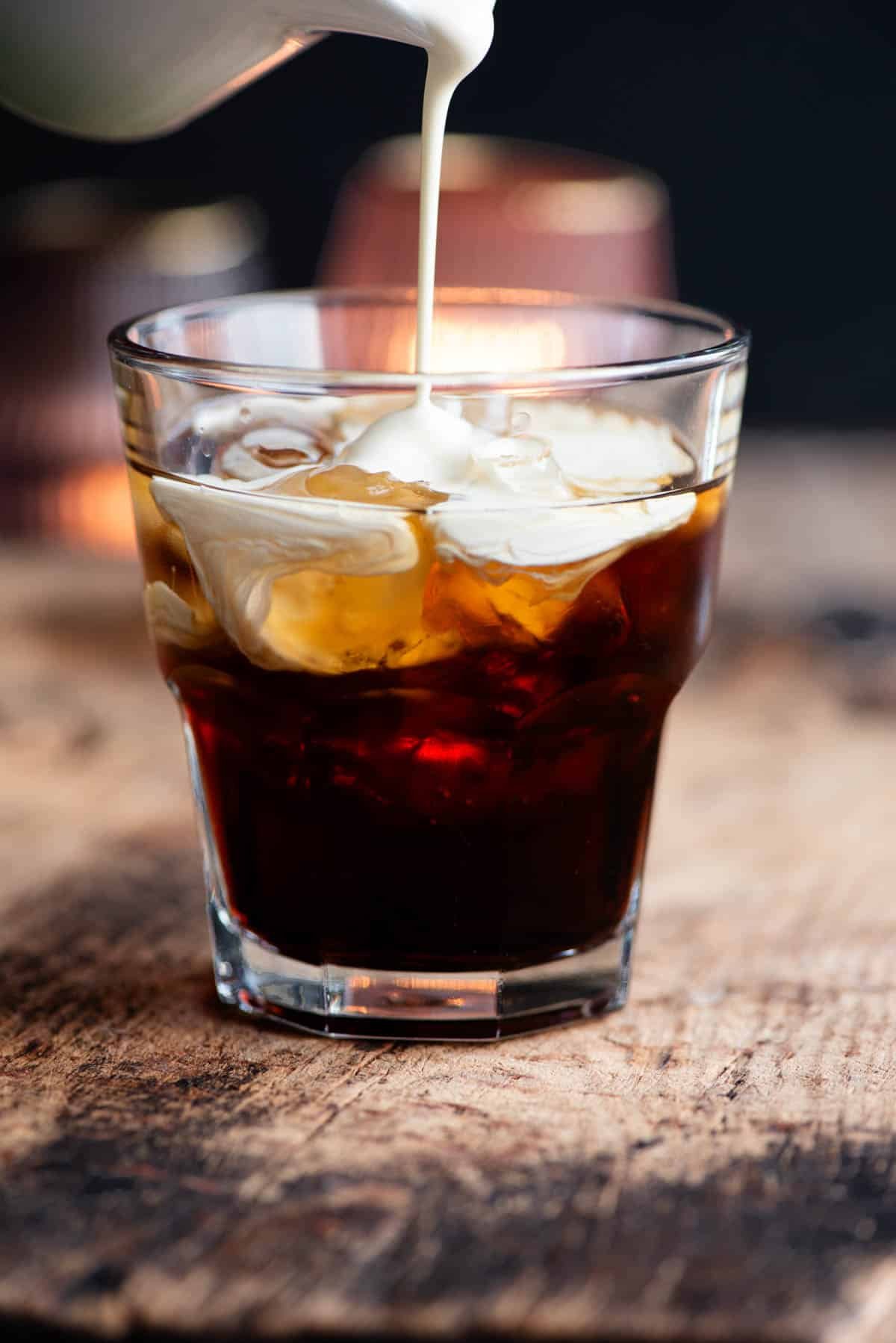 A close up of cream getting poured into a white russian cocktail.