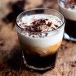 A close up cropped image of a white russian cocktail topped with chocolate shavings on a wooden table.