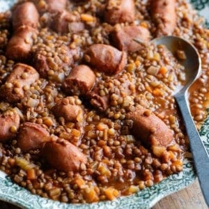 A cropped square image of Italian sausages and lentils on a serving plate.