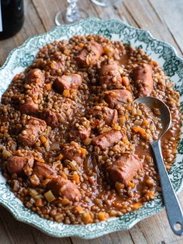 Italian sausages and lentils on a large serving plate sitting on a wooden table.